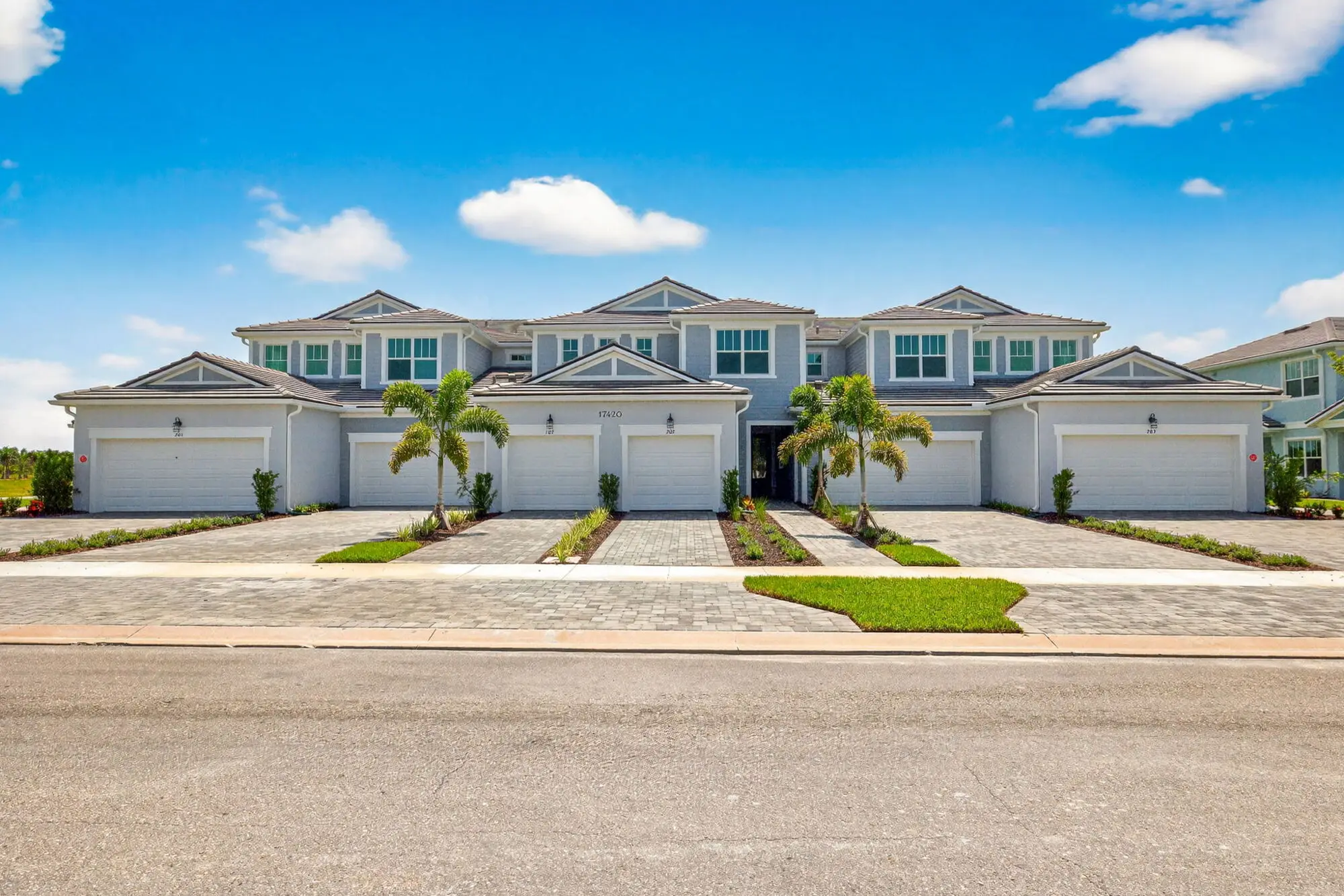 A Lakespur coach home building on Moonflower Drive, with paired garages, paver drives, and young palms under a clear sky