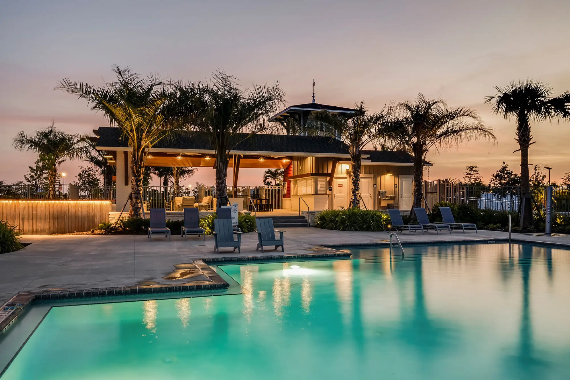 The resort pool at Lakespur at dusk, with the pavilion lit from within and lounge chairs set along the deck