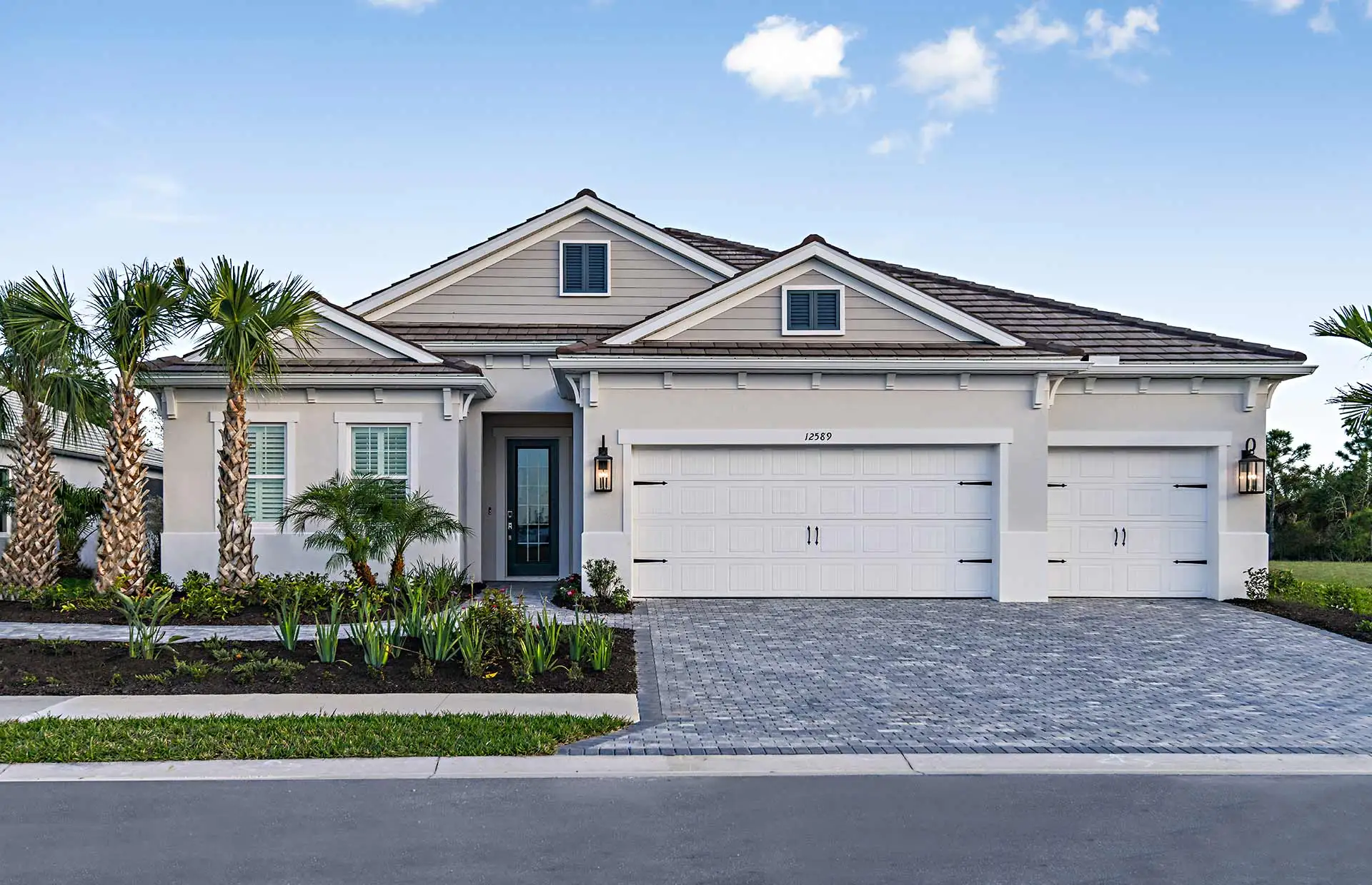 A single-story home in Avelina with a tile roof, a three-car garage, a paver driveway, and palms and planting beds across the front