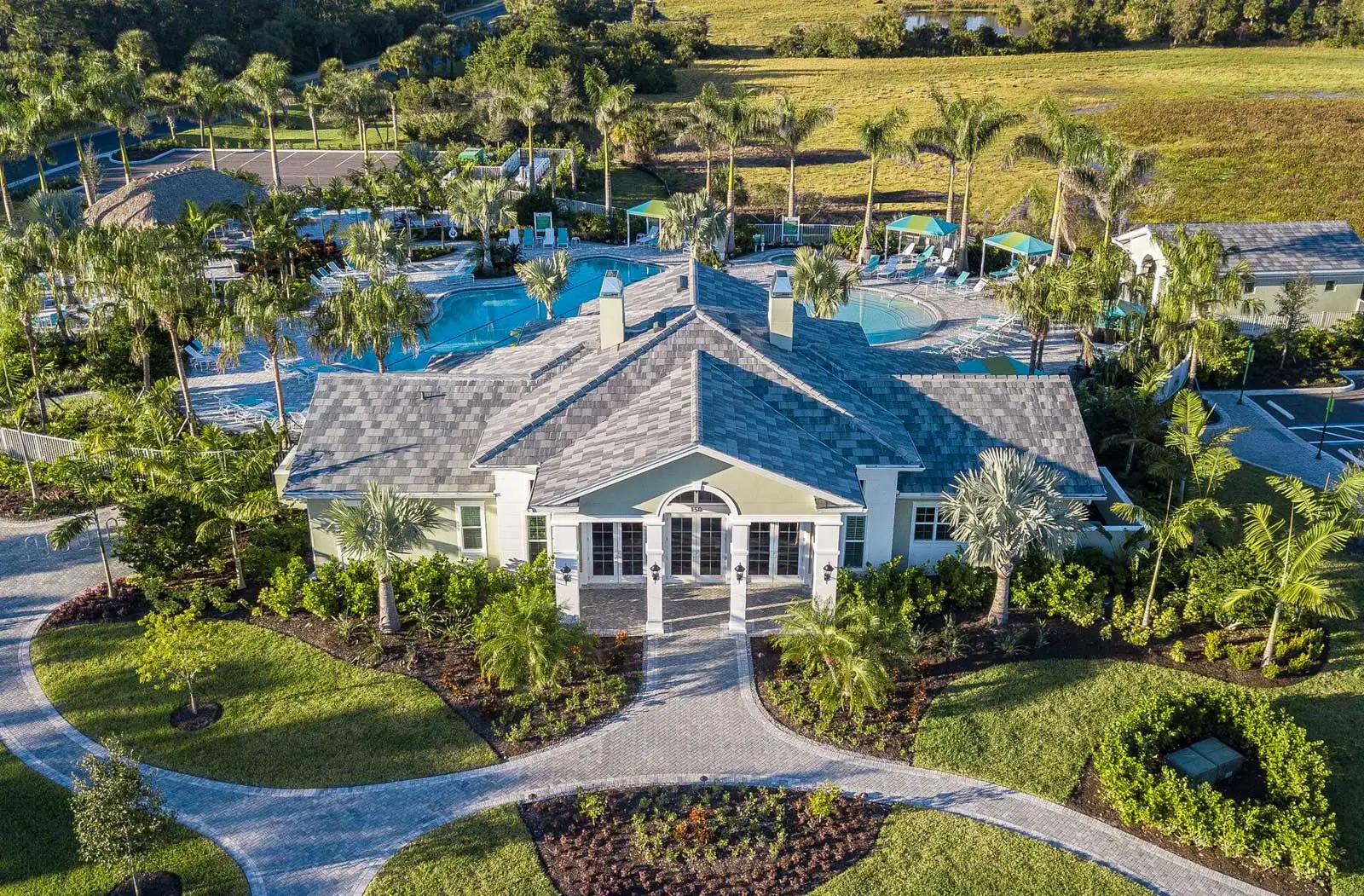Aerial view over the Boca Royale clubhouse: a paver entry drive, a resort pool and spa ringed with teal loungers and shade cabanas, and palms and preserve beyond