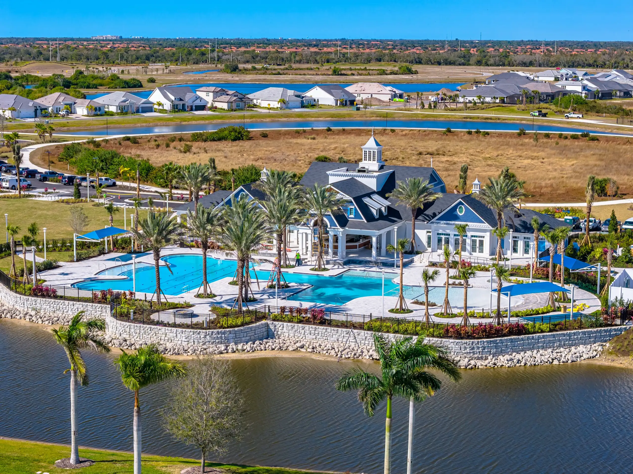 Aerial view over the Palmera clubhouse and its lakefront pools, one with swim lanes, with shade sails, homes, and open preserve beyond