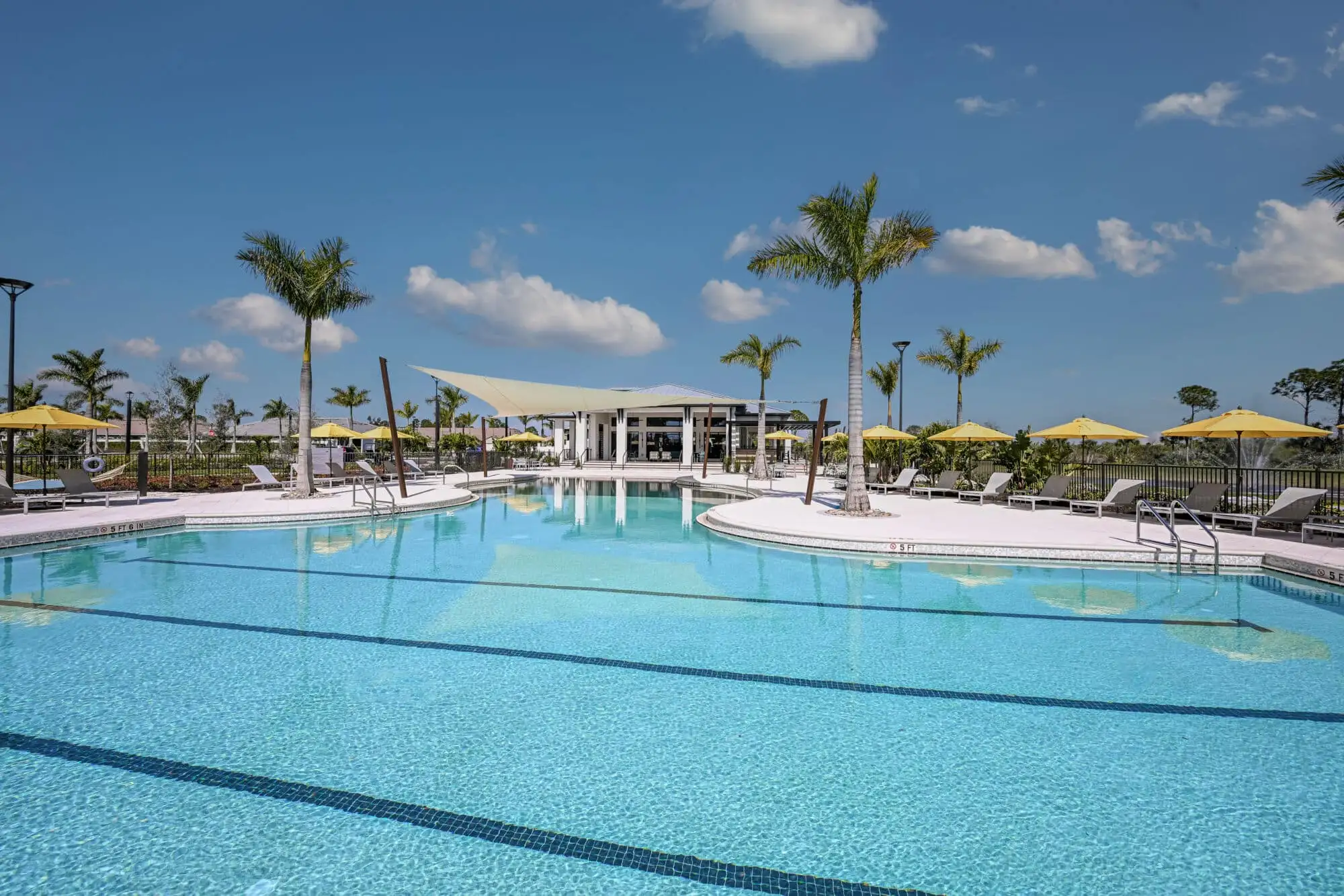 The resort pool with swim lanes at Sunstone Lakeside, edged with yellow umbrellas and loungers, with a sail-shade pavilion and palms beyond