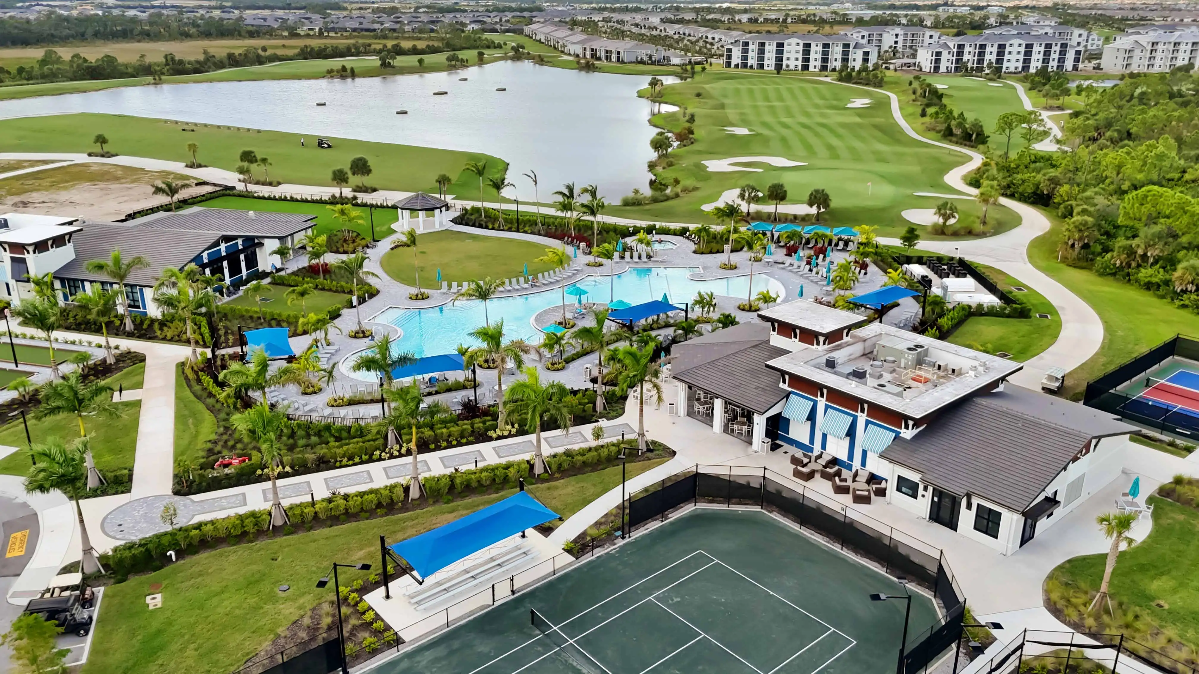 Aerial view over the Wellen Park Golf & Country Club amenity campus: resort pool, clubhouse, racquet courts, and the golf course beyond