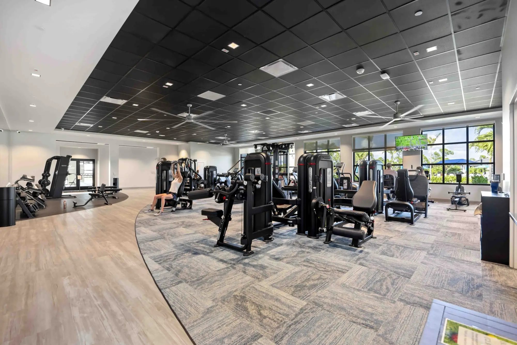 A resident using a shoulder-press machine in the fitness center at Wellen Park Golf & Country Club, with golf-course views through large windows